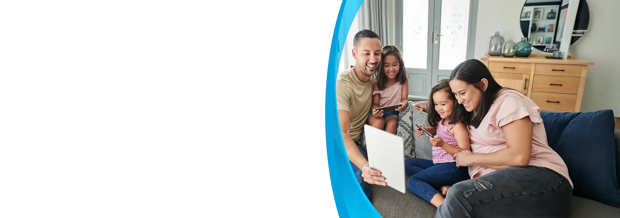 A smiling family of four shares a tablet together on a bright living room couch.